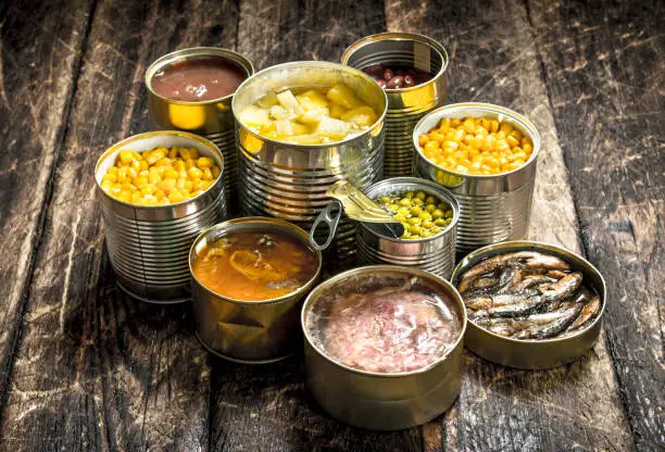 Various canned vegetables, meat, fish and fruits in tin cans. On a wooden background.
