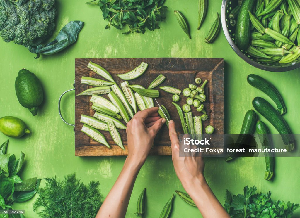 Flat-lay of healthy green vegan cooking ingredients Healthy green vegan cooking ingredients. Flay-lay of female hands cutting green vegetables and greens over green background, top view. Clean eating, vegetarian, detox, dieting food concept Vegetable Stock Photo