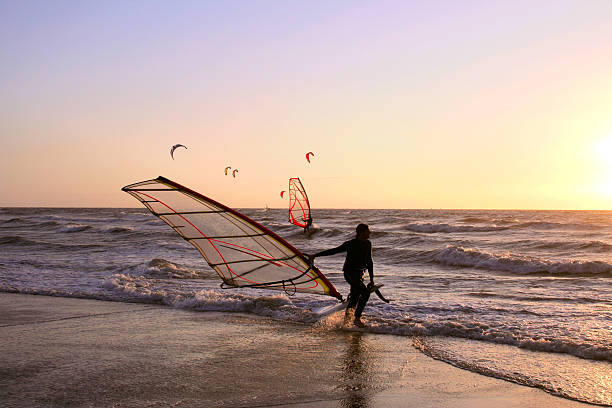 Wind surfer coming out of the surf at dusk stock photo