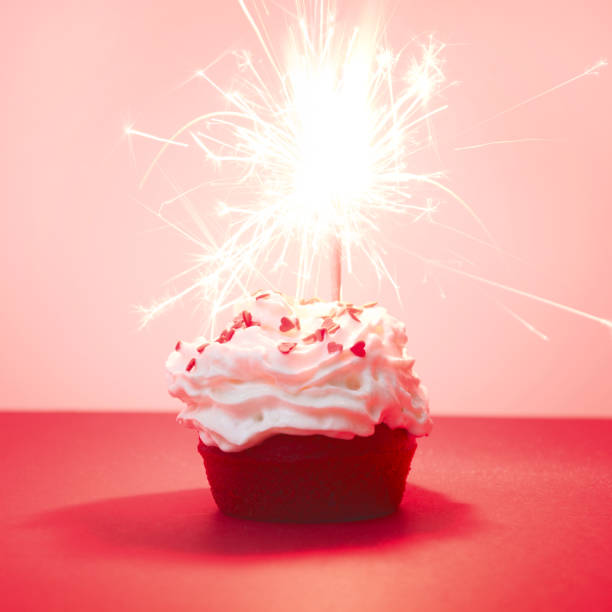 red velvet cupcake mit bengalischen lichtern auf rotem grund, rote muffin. quadratisches bild. valentinstag oder geburtstag-karte. magische funken licht. - muffin cheese bakery breakfast stock-fotos und bilder