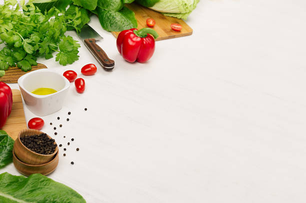 Raw fresh green vegetables, greens, red cherry tomatoes and kitchenware on soft white wood board, border. Spring vitamin dieting food.