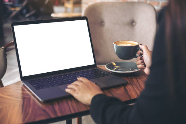 istock Mockup image of a businesswoman using laptop with blank white desktop screen while drinking hot coffee on wooden table in cafe 904102836