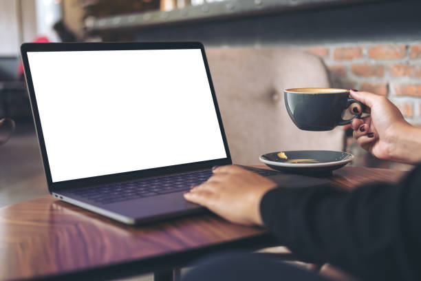 istock Mockup image of a businesswoman using laptop with blank white desktop screen while drinking hot coffee on wooden table in cafe 904102924