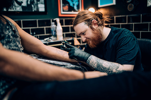 A tattoo artist tattoos a man's arm whilst wearing protective gloves.
