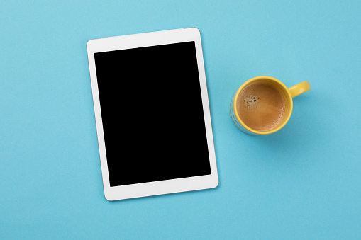 Digital tablet and coffee on blue background
