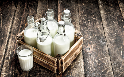 Bottles with fresh milk in a box. On a wooden background.