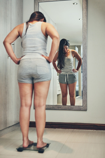 Shot of a young woman weighing herself on a scale at home