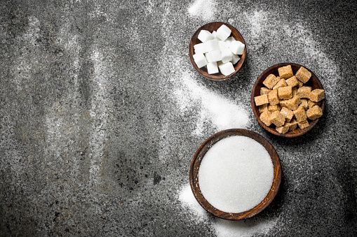 Different kinds of sugar in bowls. On a rustic background.