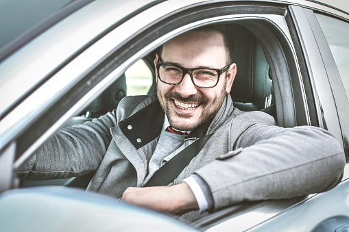 Young smiling business sitting in car and looking at camera.