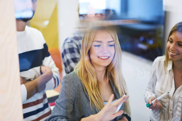 istock Crew of young positive good looking students making presentation for university seminar and writing ideas into transparent board,smiling hipster guys having fun during work break standing in office 904127546