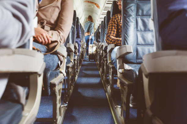 Airplane interior with people sitting on seats Interior of airplane with people sitting on seats. Passengers with suitcase in aisle looking for seat during flight. economy class stock pictures, royalty-free photos & images