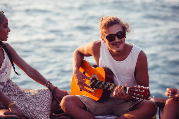 istock Man playing the guitar and relaxing on jetty with friends 904141956