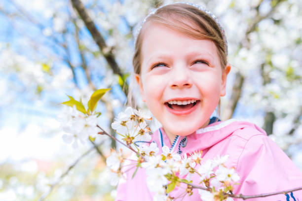 little laughing girl squinting eyes on a spring background with blooming flowers of cherries