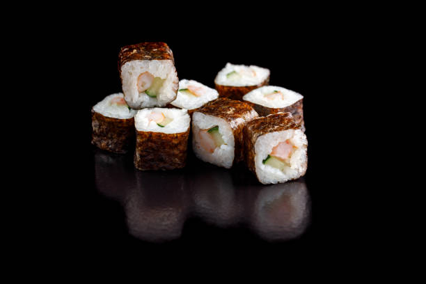 istock Classic appetizing sushi rolls with shrimp and cucumber in nori leaf on a black background close-up. 904145854