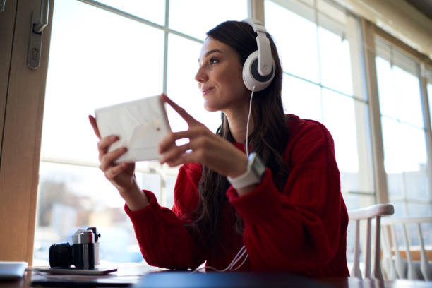 istock Charming student with smile looking out of window while watching interesting movie on website holding modern digital touch pad in hands and using free 4G internet connection in stylish loft interior 904149842
