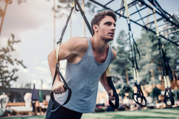 Man doing suspension training Handsome muscular man is training outdoor with suspension. Working out at gym. suspension training stock pictures, royalty-free photos & images