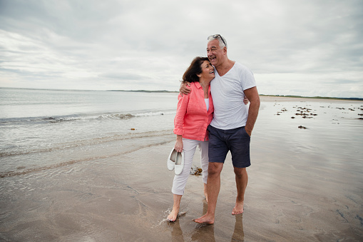A senior couple are walking along the edge of the sea on a beach