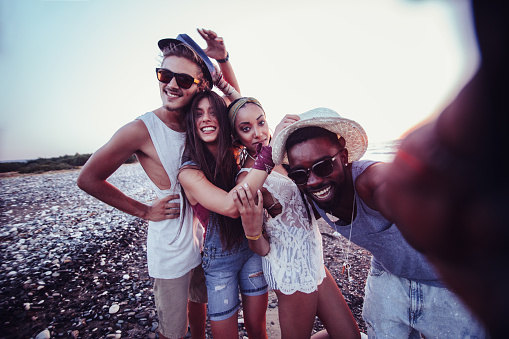 Young multi-ethnic hipster tourist friends having fun taking selfies on island beach on smartphone
