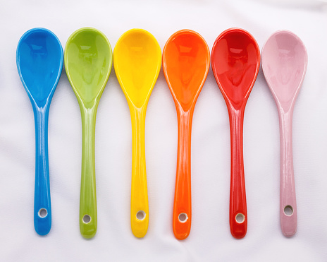 Colors ceramics spoon on white fabric background. Colorful concept.