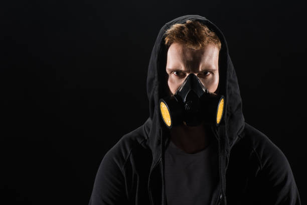 istock Man in black hood wearing protective filter mask isolated on black 904165862
