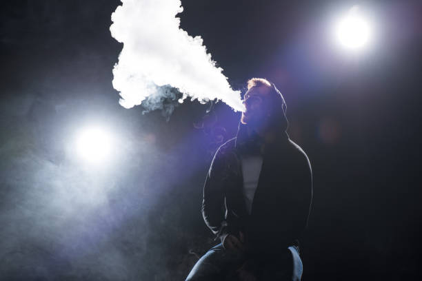 istock Young bearded man exhaling smoke of electronic cigarette against backlit 904170530