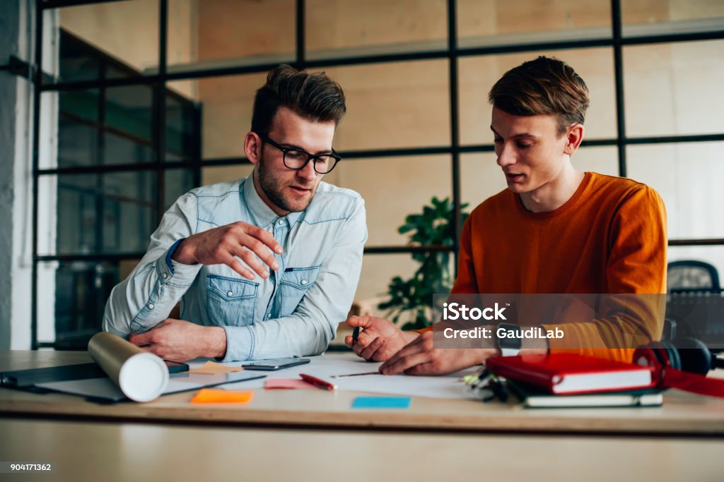 Skilled male colleagues drafting together discussing ideas for project cooperating sitting at desktop, young students brainstorming during productive job on making plan and strategy for work Creativity Stock Photo