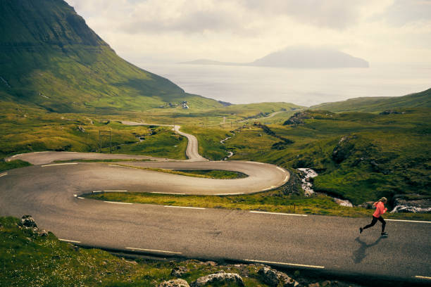 Taking my fitness outdoors Shot of a young woman running on a long, winding road in the mountains faroe islands photos stock pictures, royalty-free photos & images