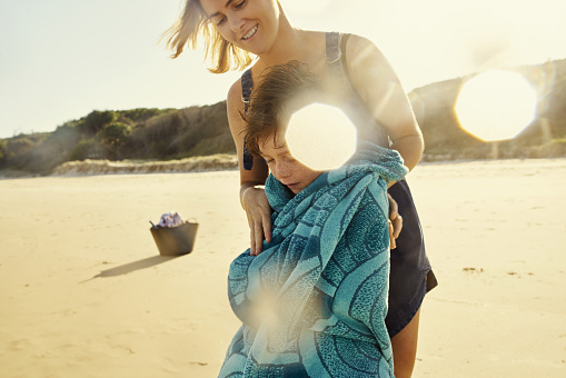 Shot of a mother wrapping her son in a towel at the beach