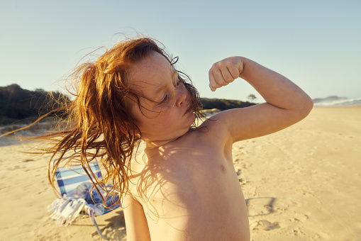 Shot of an adorable little boy flexing his muscles at the beach