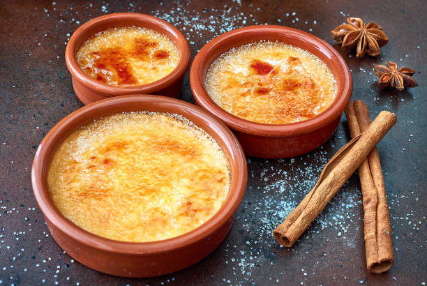 Creme brulee (cream brulee, burnt cream) in terracota baking dishes Creme brulee (cream brulee, burnt cream) in terracota cazuela dishes on old baking tray with anis stars and cinnamon sticks custard stock pictures, royalty-free photos & images