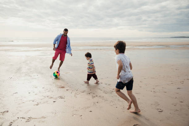 istock Father And Sons Playing With A Ball On The Beach 904206802
