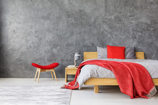 Grey spacious bedroom with king size bed with red color accents of blanket, pillow and stool