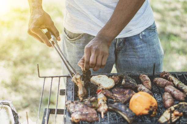 アフロ ・ アメリカ人バーベキュー - 太陽ハロー フレアと公園屋外の - 夏屋外食のコンセプト - ヴィンテージ レトロなフィルターでグリルにソーセージを入れてシェフの肉料理 - barbecue grill chef barbecue sausage ストックフォトと画像