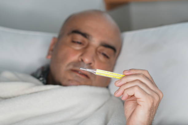 istock Sick and tired man lying in bed measuring his temperature 904223666