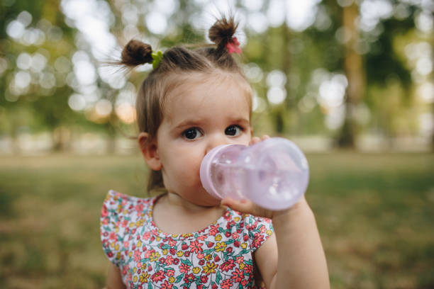One and a half year old baby girl drinking water from the baby bottle herself in the nature