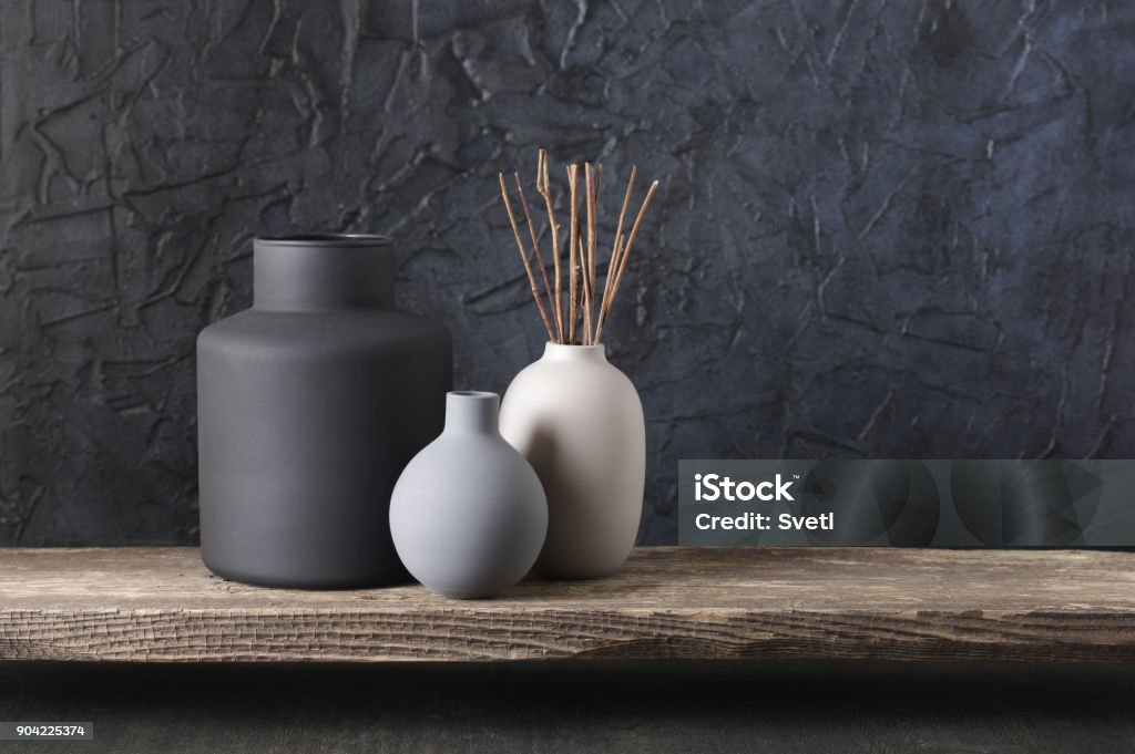 Neutral colored home decor Neutral colored vases with wood sticks on distressed wooden shelf against rough plaster black wall. Home decor. Home Decor Stock Photo