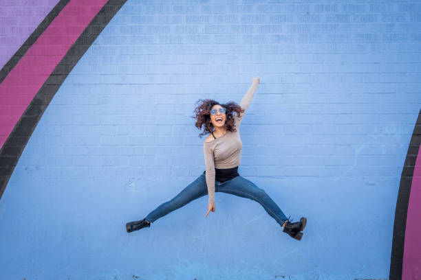 Hispanic Young woman with Positive Attitude Laughing curly haired Hispanic young woman posing against building wall. girl power photos stock pictures, royalty-free photos & images