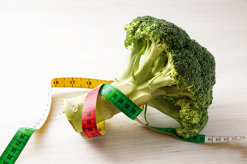 fresh broccoli and a measuring tape on a white wooden background, concept of healthy eating and slimming diet with vegetables, copy space, selected focus, narrow depth of field