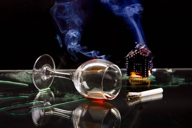 burned miniature house, overturned glass and lit cigarette