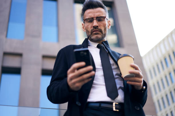 istock Selective focus, handsome 40 years successful businessman with smartphone using 4G wireless connection sending important message. Businessman using cellular near office building with coffee take away 904250140