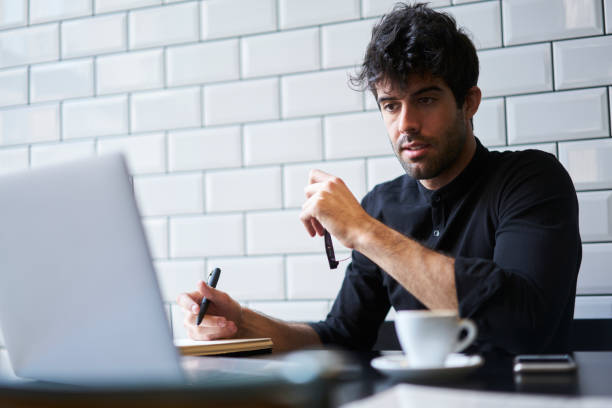 istock Smart male student watching webinar about developing business ideas on modern laptop and noting important information in notebook for future using sitting in coworking space with free 4G internet 904254596