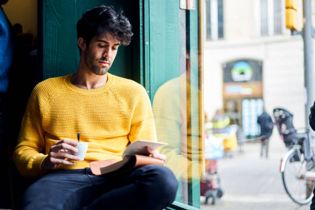 istock Young skilled male trainee of journalist editorship holding notebook rereading press release correcting mistakes in text before sending it to professional coach sitting with cup of espresso in cafe 904254718