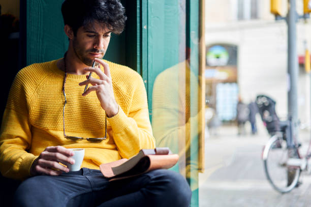 istock Thoughtful handsome Spanish guy creating motivating checklist of plans for year noting important events and goals must be achieved to become successful drinking coffee and holding smartphone in cafe 904256904