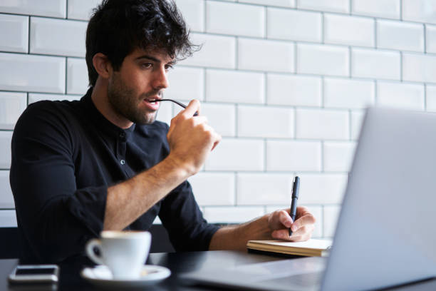 istock Young male businessman with eyeglasses thinking about building plan on future year using free internet connection on computer and noting every step in notebook while drinking coffee in cafe 904256960