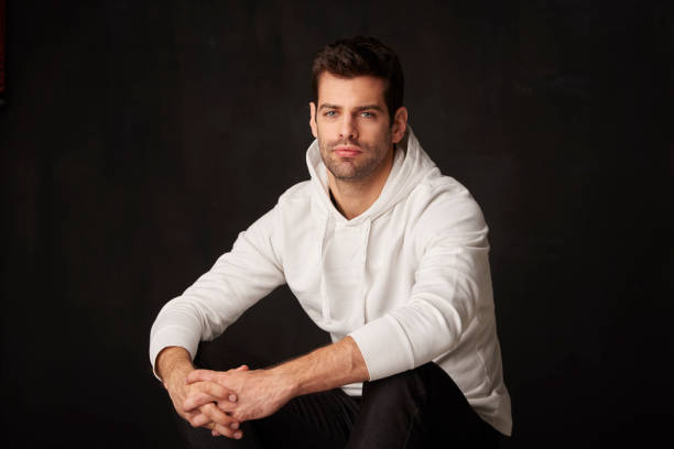istock Studio shot of a handsome young man sitting at dark background while looking at camera and smiling. 904257706