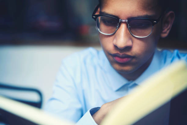 close up retrato de joven estudiante internacional hombre inteligente en gafas leyendo interesantes página turner novela del famoso autor gasto ocio hobby admirar emocionante trama y personajes - page turner fotografías e imágenes de stock