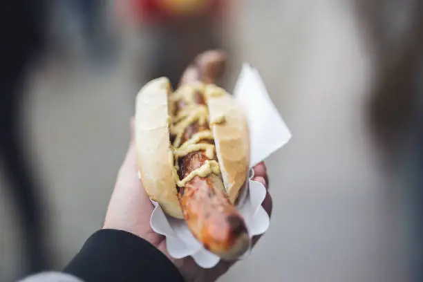 Arm of an adult man holding a hot dog with a sausage covered in mustard.
