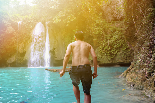 Young man moving forward to jump off the pond in waterfall scenery background