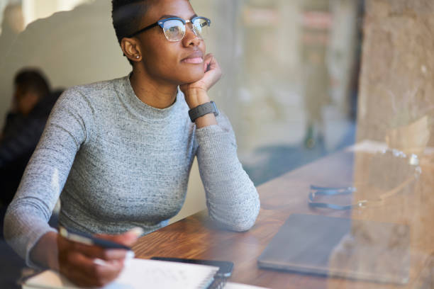 charmante jeune afro américain créatif écrivaine en lunettes de soleil et de la pensée de tenue casual élégant au fil de l’intrigue pour nouvelle histoire en notant les idées dans le journal tout en dépensant temps libre dans l’espace de coworking moderne - lundi noir chinois photos et images de collection