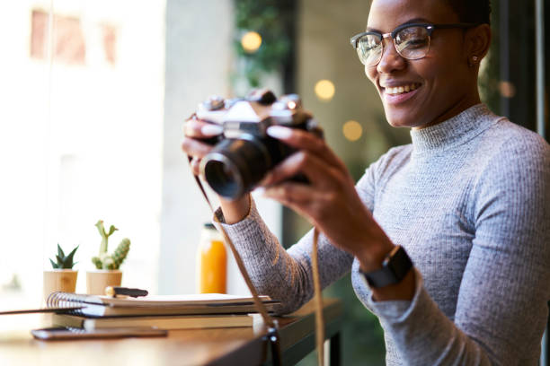 joyeux séduisante jeune afro américain photographe professionnel dans les verres élégants et branché tenue de faire des photos pour la session de photo rétro en utilisant l’appareil photo vintage travaillant à l’intérieur en studio moderne - lundi noir chinois photos et images de collection